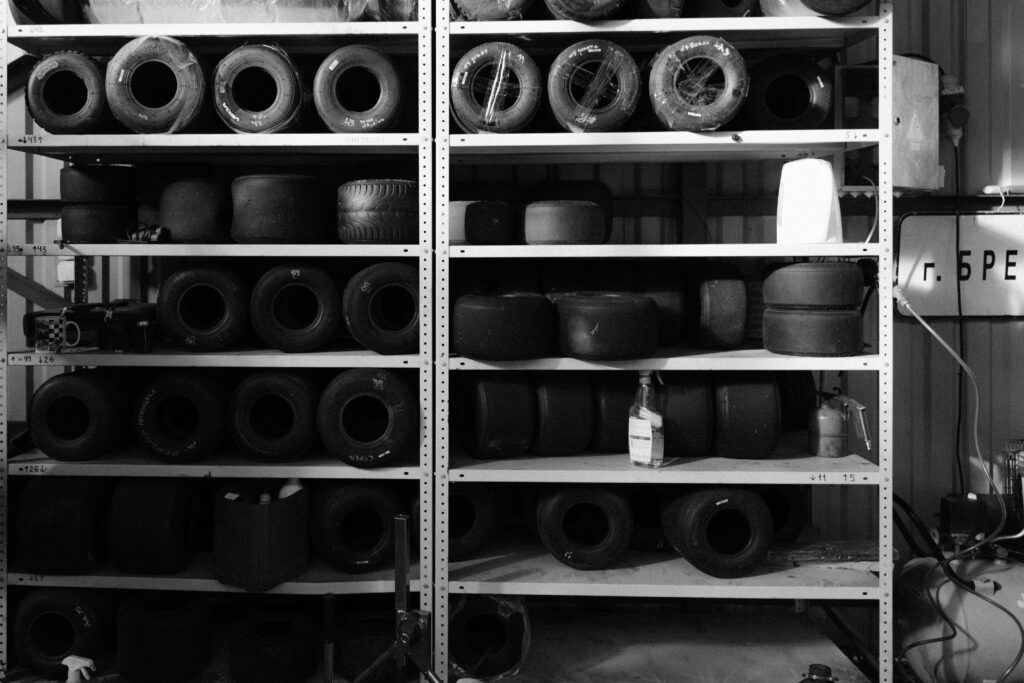 Monochrome image of stacked go-kart tires on sturdy shelves, showcasing various wheel sizes.